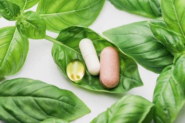 Pilules et feuilles vertes sur fond blanc, concept de naturopathie — Photo de stock