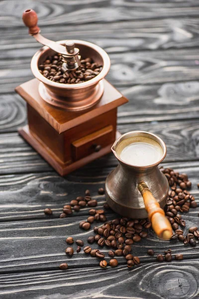 Foco seletivo de moedor de café vintage com grãos de café perto cezve na superfície de madeira — Fotografia de Stock