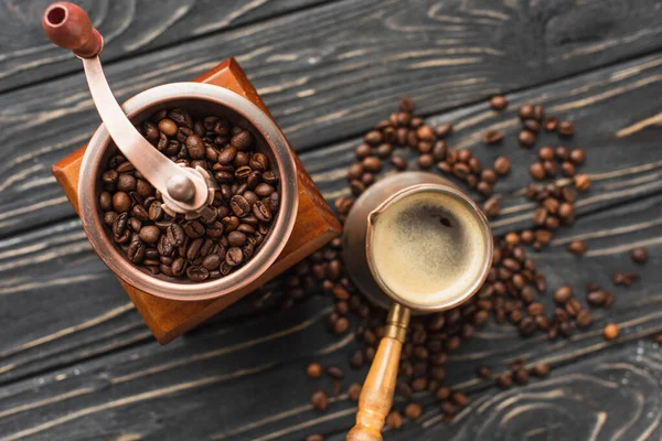 Top view of vintage coffee grinder with coffee beans near cezve on wooden surface — Stock Photo