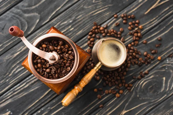 Top view of vintage coffee grinder with coffee beans near cezve on wooden surface — Stock Photo