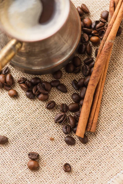 Close up view of cezve with coffee near cinnamon sticks and coffee beans on sackcloth — Stock Photo