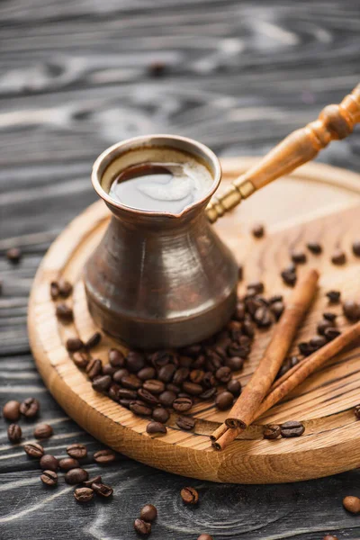 Selective focus of cezve with coffee near cinnamon sticks on wooden board — Stock Photo