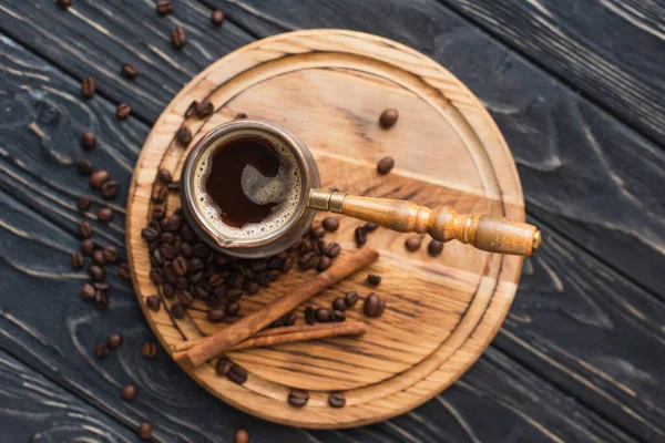 Vue de dessus de cezve avec café près bâtons de cannelle sur planche en bois — Photo de stock