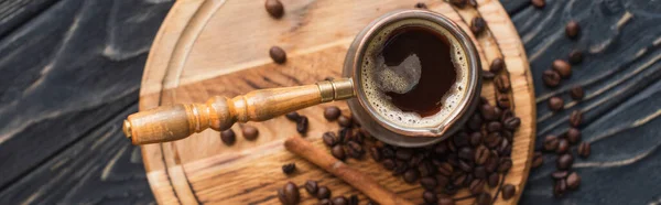 Top view of cezve with coffee near cinnamon stick on wooden board, panoramic shot — Stock Photo