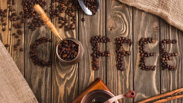 Draufsicht auf Kaffee-Schriftzug aus Bohnen und Cezve auf Holzoberfläche — Stockfoto