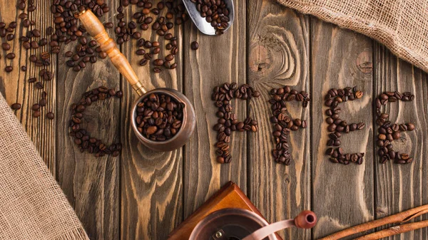 Vista superior de letras de café hechas de frijoles y cezve en la superficie de madera - foto de stock