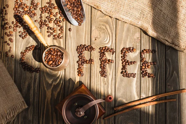 Vue du dessus de lettrage de café en grains et moulin à café avec cezve à la lumière du soleil sur la surface en bois — Photo de stock