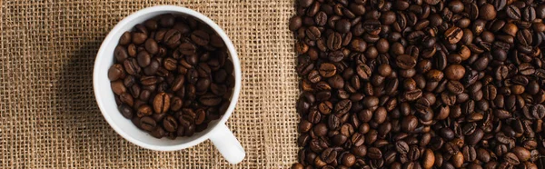 Vista dall'alto di tazza con chicchi di caffè e sacco su sfondo, colpo panoramico — Foto stock