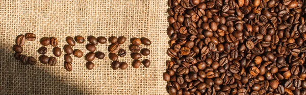 Top view of coffee lettering made of beans in sunlight on sackcloth, panoramic shot — Stock Photo