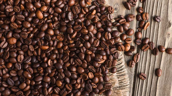 Vue de dessus des grains de café éparpillés sur la toile de jute sur la surface en bois — Photo de stock