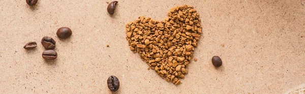 Top view of heart made of instant coffee near coffee beans on beige surface, panoramic shot — Stock Photo