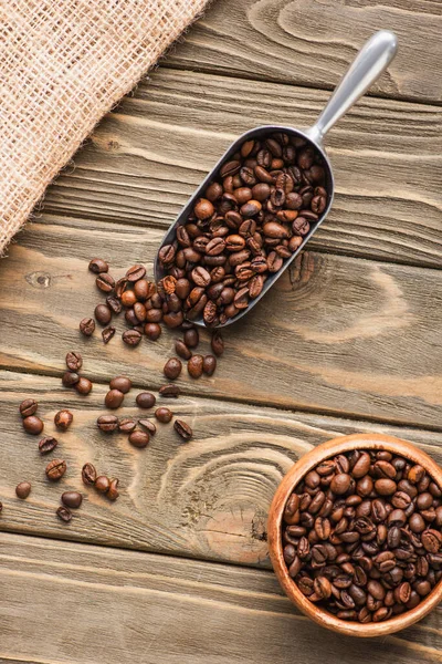 Vista superior del saco, cucharada de metal con granos de café y tazón en la superficie de madera - foto de stock