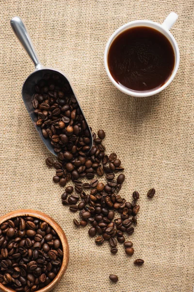 Draufsicht auf Tasse, Metalllöffel mit Kaffeebohnen und Schale auf Sacktuch — Stockfoto