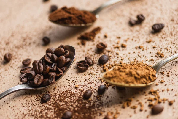 Messa a fuoco selettiva di caffè macinato, istantaneo e fagioli in cucchiai su superficie beige — Foto stock