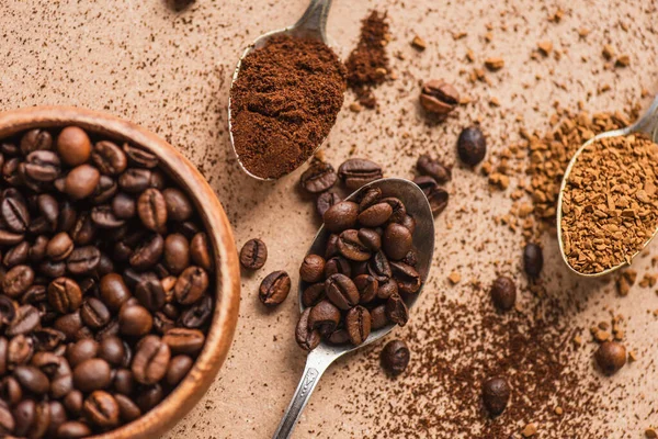 Vista dall'alto di terra, caffè istantaneo e fagioli in cucchiai vicino alla ciotola di legno sulla superficie beige — Foto stock