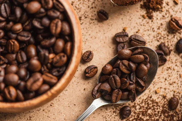 Top view of coffee beans in spoon and wooden bowl on beige surface — Stock Photo