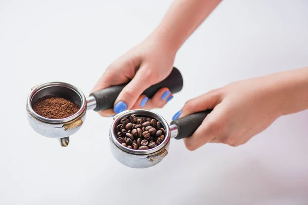 Vista cortada de barista segurando portafilters com grãos de café e café moído sobre fundo branco — Fotografia de Stock