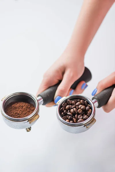 Vista cortada de barista segurando portafilters com grãos de café e café moído sobre fundo branco — Fotografia de Stock