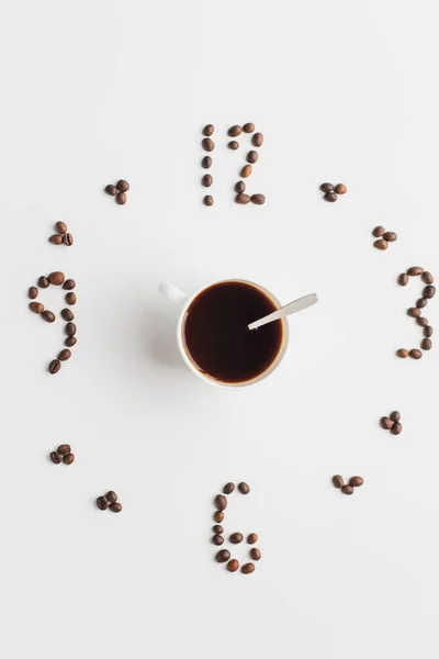 Верхний вид часов из кофейных зерен вокруг чашки на белой поверхности — стоковое фото