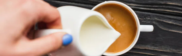 Vista recortada de barista añadiendo leche al café en taza sobre superficie de madera, plano panorámico - foto de stock