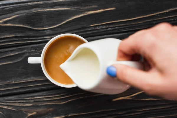 Vista ritagliata di barista aggiungendo latte al caffè in tazza sulla superficie di legno — Foto stock