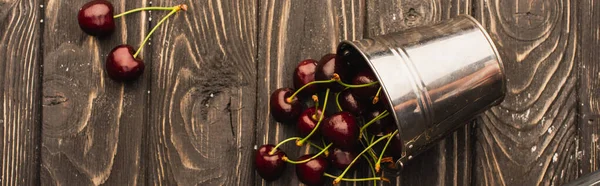 Vue de dessus des cerises douces mûres dispersées du seau en métal sur la surface en bois, vue panoramique — Photo de stock