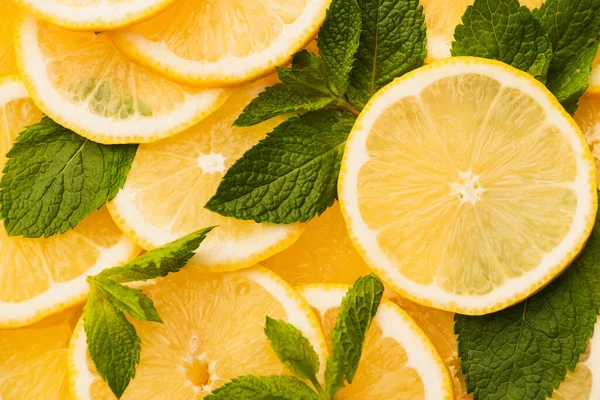 Вид сверху на нарезанные желтые лимоны с мятными зелеными листьями — стоковое фото
