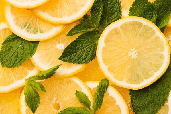 Vue de dessus des citrons jaunes tranchés avec des feuilles vertes menthe — Photo de stock