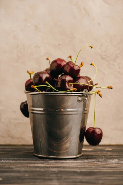 Cerises douces mûres humides dans un seau métallique sur une surface en bois — Photo de stock