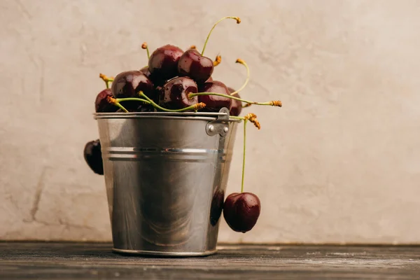 Wet ripe sweet cherries in metal bucket on wooden surface — Stock Photo