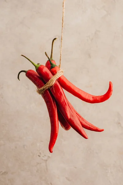 Bunch of red chili peppers tied with rope hanging on beige concrete background — Stock Photo