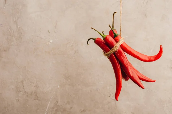Bunch of red chili peppers tied with rope hanging on beige concrete background — Stock Photo