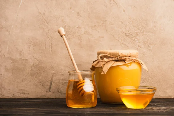 Sweet honey in glass jars with stick on wooden surface near beige concrete wall — Stock Photo