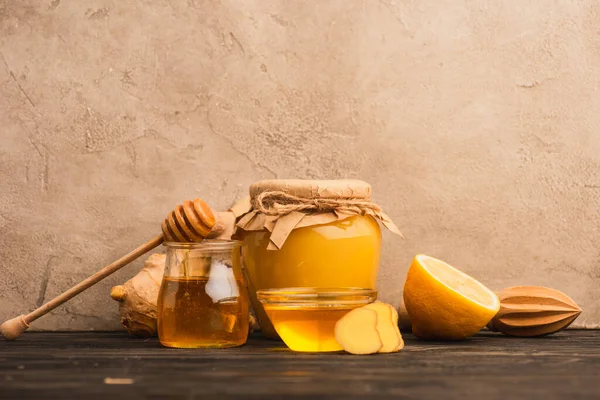Süßer Honig, Ingwerwurzel und Zitrone auf Holzfläche nahe beiger Betonwand — Stockfoto