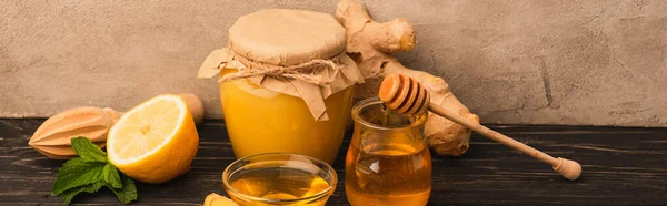 Miel dulce, hojas de menta, raíz de jengibre y limón en la superficie de madera cerca de la pared de hormigón beige - foto de stock