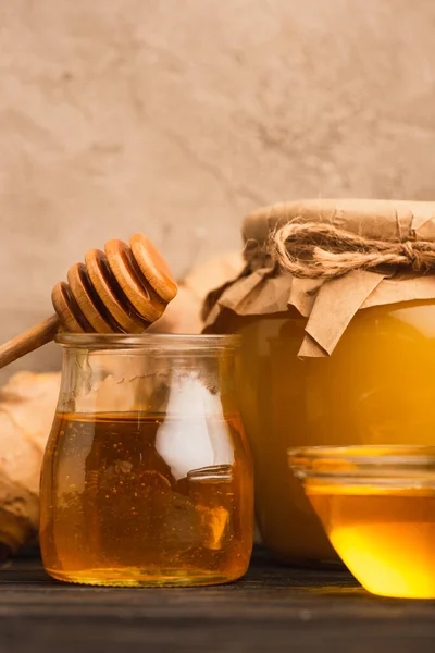 Vista de cerca de la miel dulce en frascos de vidrio con palo en la superficie de madera cerca de la pared de hormigón beige - foto de stock