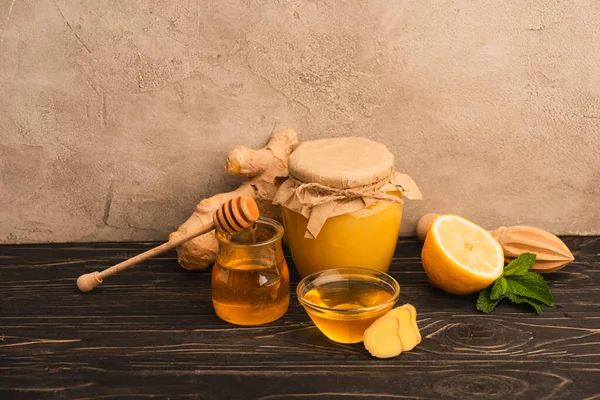 Süßhonig, Minzblätter, Ingwerwurzel und Zitrone auf Holzoberfläche nahe beiger Betonwand — Stockfoto