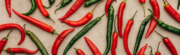 Top view of red chili peppers and green jalapenos on beige concrete surface, panoramic shot — Stock Photo