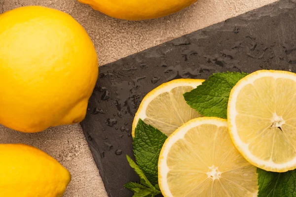 Top view of mint green leaves, lemon slices on black board on beige concrete surface — Stock Photo