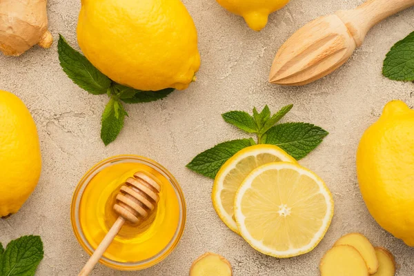 Top view of yellow lemons with mint green leaves, ginger root slices and honey on beige concrete surface — Stock Photo