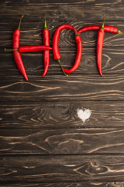 Vista superior de la palabra picante hecha de chiles cerca del corazón de sal en la superficie de madera - foto de stock