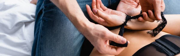 Panoramic crop of man tying hands of woman with lace ribbon — Stock Photo