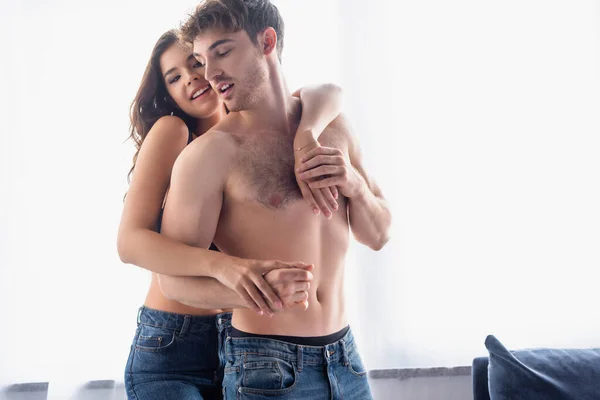 Giovane donna bruna che abbraccia il fidanzato senza maglietta a casa — Foto stock