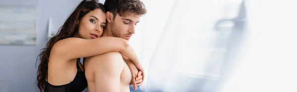 Orientation panoramique de la jeune femme en soutien-gorge étreignant petit ami torse nu et regardant la caméra — Photo de stock