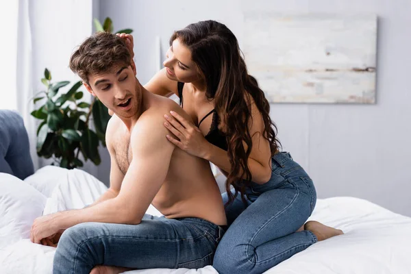 Mulher em jeans sentado na cama perto de namorado muscular — Fotografia de Stock