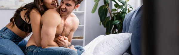 Récolte horizontale de femme en jeans et soutien-gorge assis sur le lit avec petit ami musclé — Photo de stock