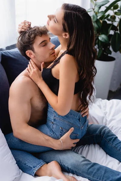 Brunette woman in jeans sitting on shirtless man with closed eyes — Stock Photo