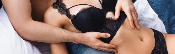 Panoramic crop of man hugging seductive woman in bra lying on bed — Stock Photo