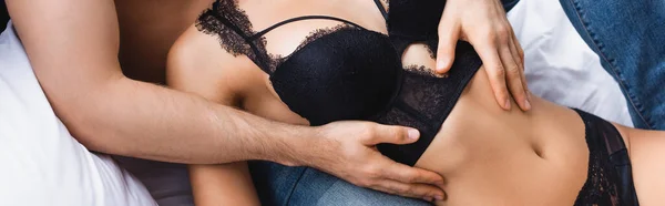 Récolte panoramique de l'homme étreignant femme séduisante en soutien-gorge couché sur le lit — Photo de stock