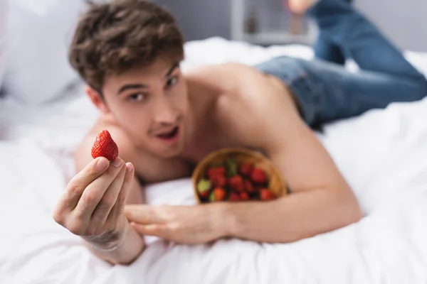 Messa a fuoco selettiva di uomo senza camicia sdraiato sul letto e tenendo fragola rossa — Foto stock